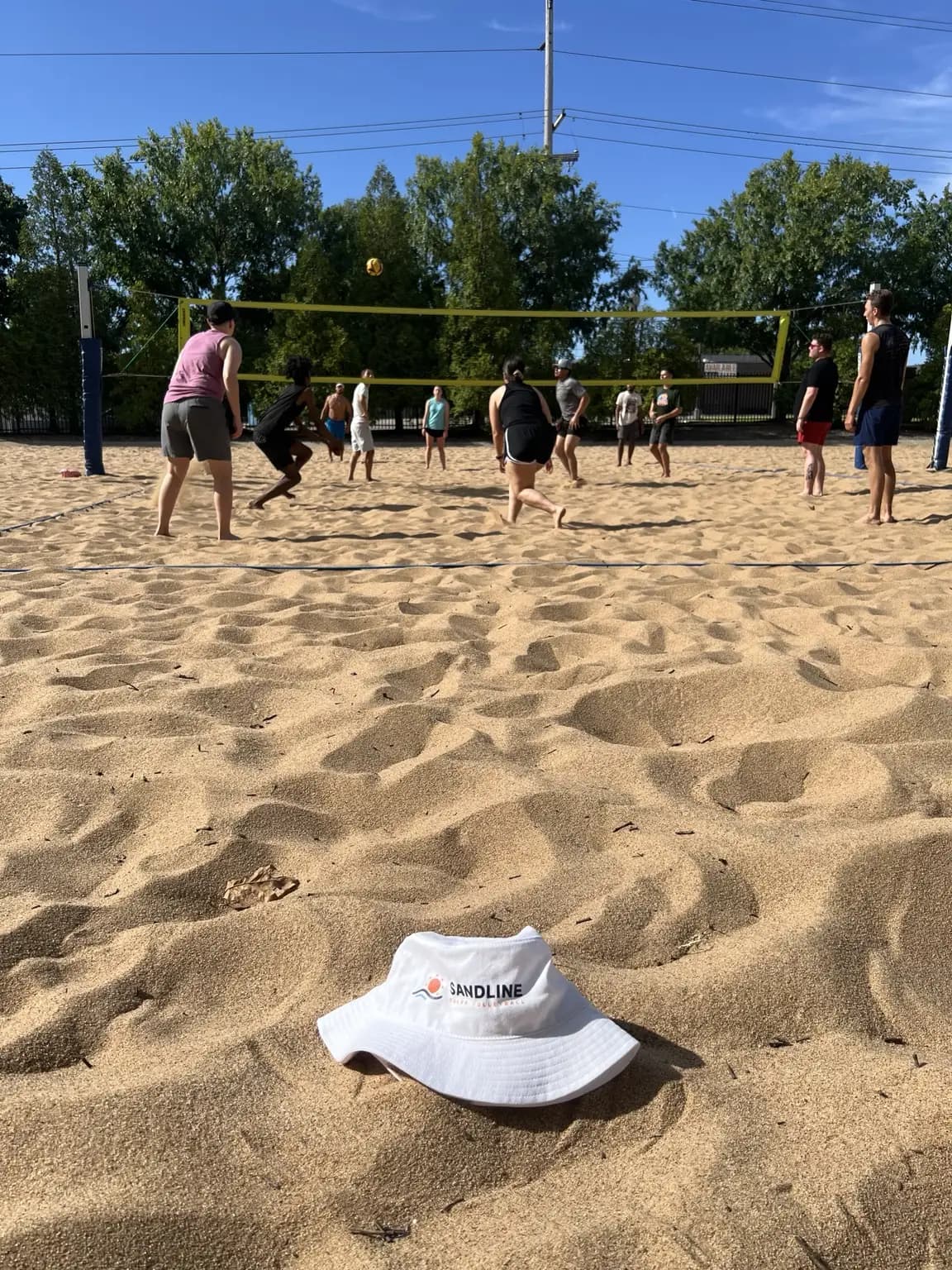 A white Sandline bucket hat rests on the sand with pickup action in the background